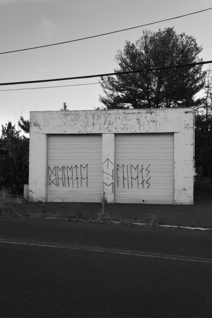 Black and white photograph of some kind of garage with indecipherable graffiti on it.