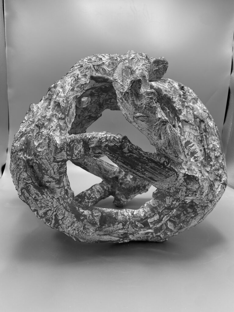 Grayscale sculpture of a round, hollow object. It has a rough and bumpy texture.