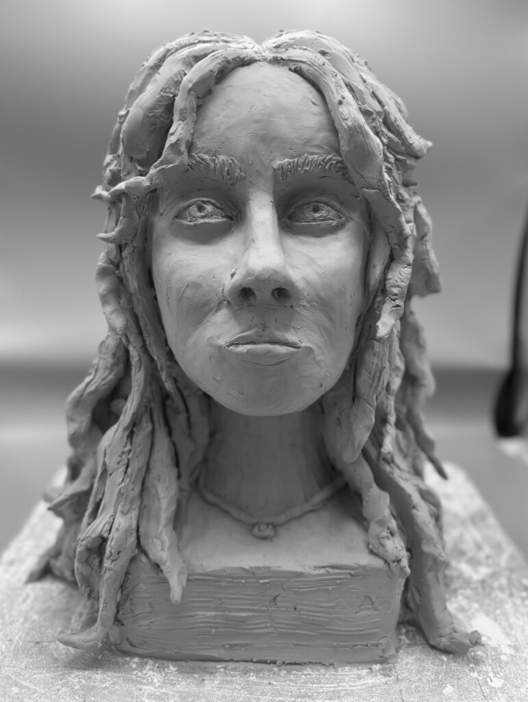 Sculpture of a girl's head. She has long thick hair and a necklace.