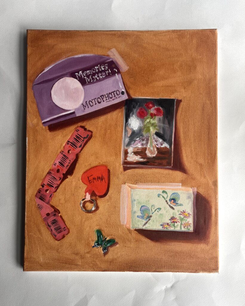 Oil painting of various items: a MotoPhoto camera, a smaller oil painting of roses in a vase, several red tickets, a heart keychain with the name Emma on it, a small green butterfly, and some kind of rectangular object with butterflies and flowers on it.